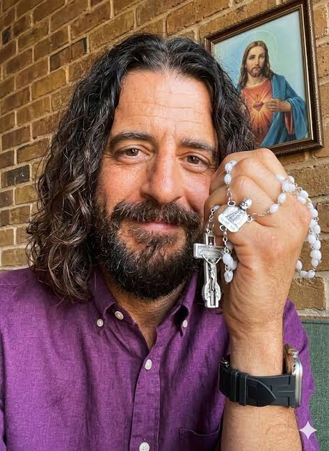 Jonathan Roumie holding a white-bead commemorative rosary